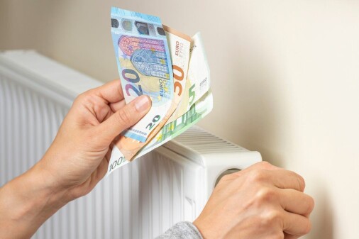 Zwei Hände, die rechte dreht die Regulierung an einem Heizkörper, die andere hält Euroscheine.