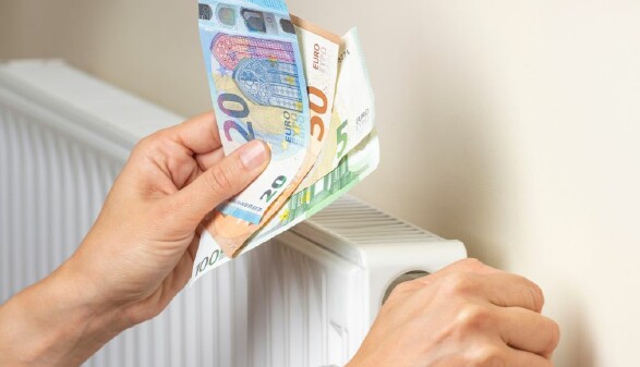 Zwei Hände, die rechte dreht die Regulierung an einem Heizkörper, die andere hält Euroscheine.